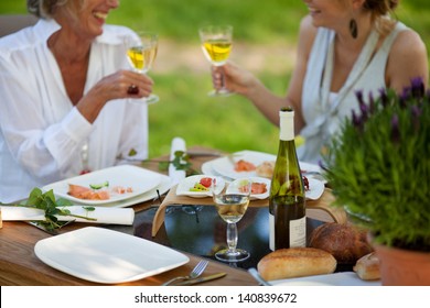 Two Women Saying Cheers At Dining Table Outdoors