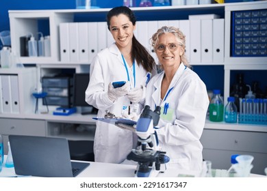 Two women scientists using smartphone working at laboratory - Powered by Shutterstock