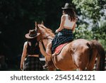 Two women are seen horseback riding, enjoying a sunny day in the outdoors while wearing cowboy hats. The scene portrays relaxation and adventure in nature.