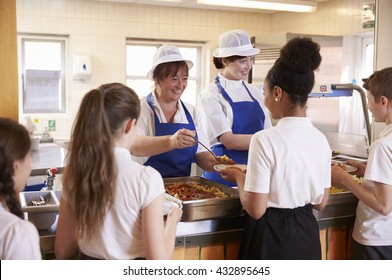 Two Women Serving Kids Food In A School Cafeteria, Back View