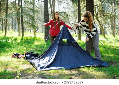 Two women are setting up a tent in a forest. Scene is peaceful and serene, as the women are surrounded by nature and the trees - Powered by Shutterstock