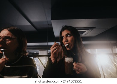 Two women share a moment over drinks in a dimly lit bar with soft glowing lights in the background, depicting friendship and relaxation. - Powered by Shutterstock