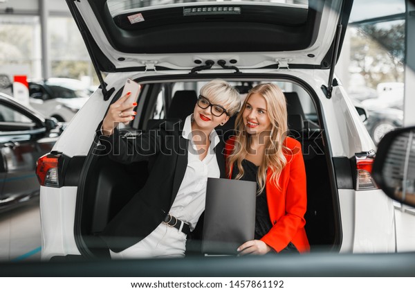Two women sitting in the back of car\
and making a selfie on a smartphone . -\
Image