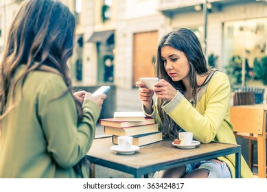 Two Women Sitting In A Bar And Staring At Mobile Phones - Girls Watching A Video Online On Portable Device