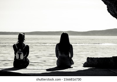 Two Women Sitting By The Seaside, Distance Between Them.Body Language Drifting Apart, Black And White