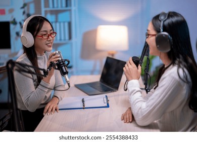 Two women are sitting at a desk with microphones and a laptop. They are recording a podcast. Scene is professional and focused - Powered by Shutterstock