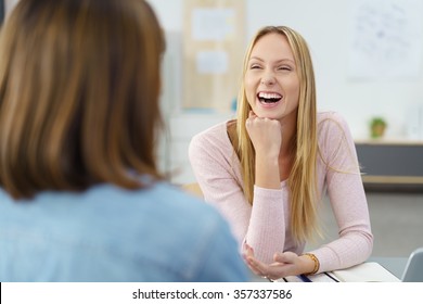 two women sitting at a desk, talking and laughing together