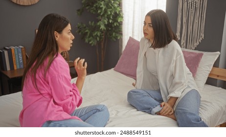 Two women sitting on a bed having a serious conversation in a cozy bedroom, indicating a setting of friendship, intimacy, and trust. - Powered by Shutterstock