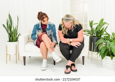 Two Women Sitting On Couch Listening To Headphones Holding Phones