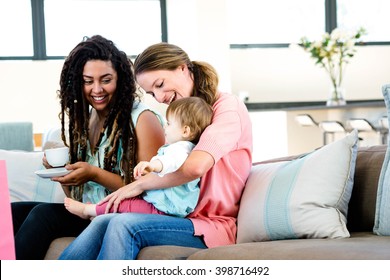 Two Women Sitting On A Couch Smiling At An Adorable Baby