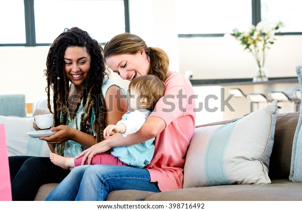 Two women sitting on a couch smiling at an adorable baby