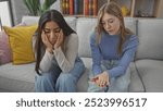 Two women sitting on a sofa in a living room, one comforting the other who appears upset.