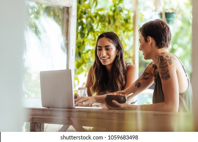 Two women sitting at a restaurant working on a laptop computer. Women sitting at a restaurant enjoying desserts. - Powered by Shutterstock