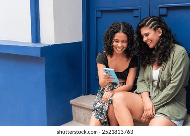 Two Women Sitting and Smiling While Looking at Smartphone