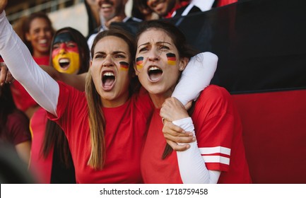 Two women sitting in stadium with face painted in german flag colors yelling from fan zone. Females from Germany cheering from stadium fan zone. - Powered by Shutterstock