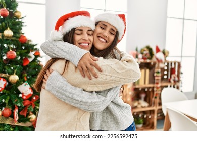 Two women smiling confident hugging each other standing by christmas tree at home - Powered by Shutterstock