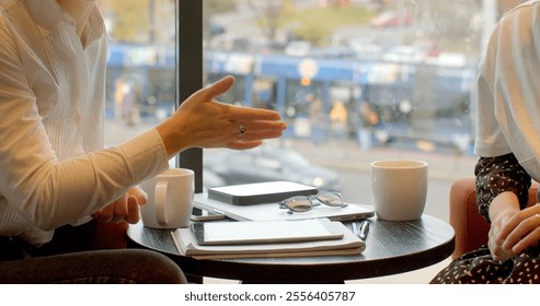 Two Women Solving Business Tasks with Tablets in Casual Cafe Atmosphere. Hands close-up gesturing focusing on communication, body language, or expression. Conveying messages effectively, lifestyle.