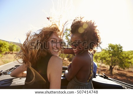 Two women standing in the back of open car turning to camera