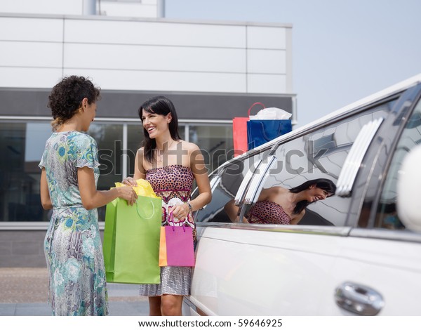 two women standing by\
limousine and looking at shopping bags. Horizontal shape, copy\
space