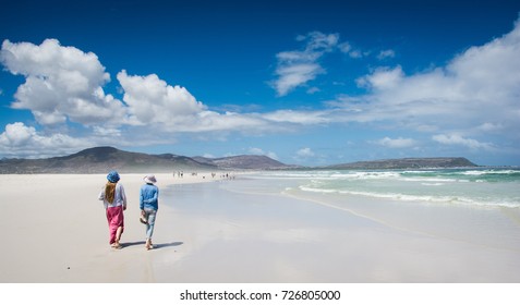 Two women strolling under summer skies on a white beach 