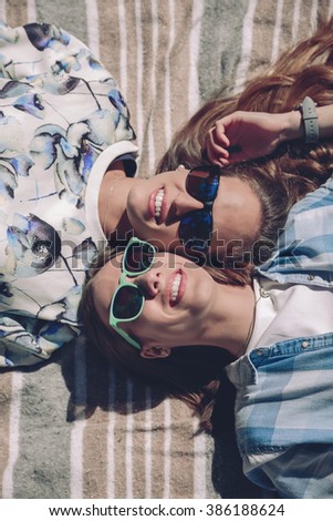 Two women with sunglasses smiling lying in blanket