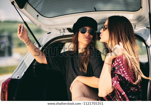 Two women taking selfie while sittink in a\
trunk. Road rtip concept.
