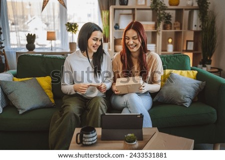two women teenage friends or sisters receive presents in box open read card happy smile in front of digital tablet at home online video call