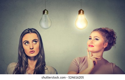 Two women thinking looking up at light bulbs isolated on grey wall background. Human face expressions, emotions, perception. Cognitive skills ability concept