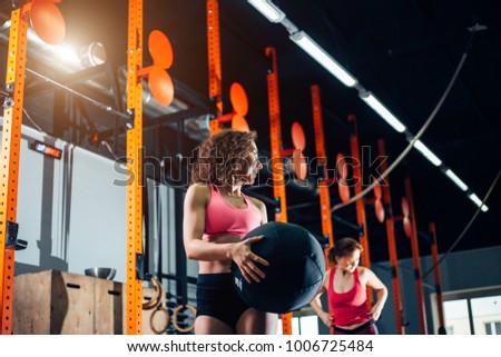 Two women throws medicine balls in fitness gym