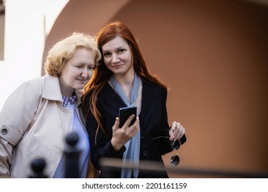 Two women together - blonde in light and redhead in dark clothes read a message on a smartphone. 
Cosplay - female version of Angel and Demon (Good Omens) - Shutterstock ID 2201161159