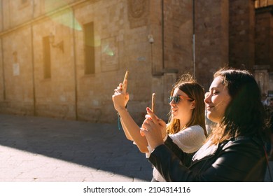 Two Women Tourist Visiting An Ancient City In Spain Taking A Picture Of A Salamanca Monument With Her Mobile Phone At Sunset. Focus On Second Girl