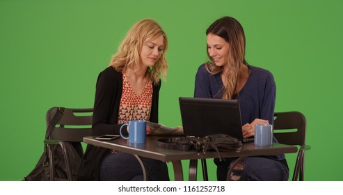 Two Women Using Map And Laptop At Cafe To Pick Destination On Green Screen