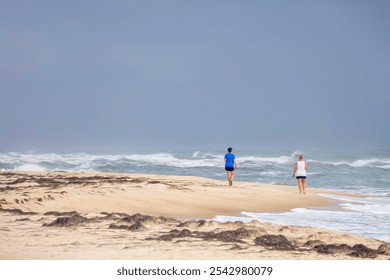 Two women walk along sandy beach of a barrier island, with a view of breaking surf in the Gulf of Mexico, on a windy autumn afternoon in the Florida Panhandle. Light digital oil-painting effect. - Powered by Shutterstock