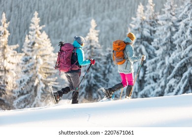 Two women walk in snowshoes in the snow, winter trekking, two people in the mountains in winter, hiking equipment - Shutterstock ID 2207671061