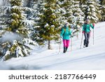 Two women walk through the snow on a winter hike, two in the mountains in winter, hiking equipment, snowshoes
