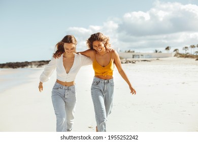 Two women walking together at the beach, hugging each other and smiling - Friends enjoying their vacation at the sea - Women wearing casual clothes - Powered by Shutterstock