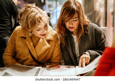 Two Women Wearing Coats Choosing Foods On Outdoor Cafe Or Resturant Menu.