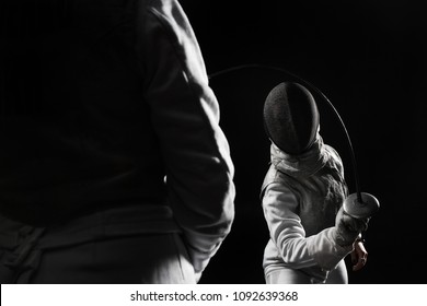 Two Women Wearing Helmets And White Uniforms Fencing On Black Background