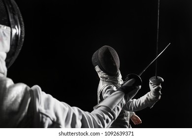 Two Women Wearing Helmets And White Uniforms Fencing On Black Background