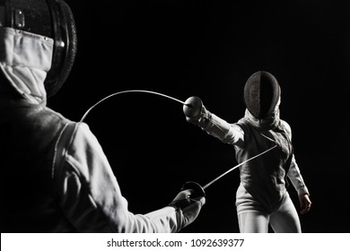 Two Women Wearing Helmets And White Uniforms Fencing On Black Background