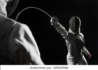 Two Women Wearing Helmets And White Uniforms Fencing On Black Background