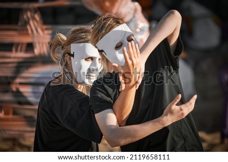Two women in white theatre mask dancing on art theatrical festival. Outdoor dance performance of two girls dancers in total black clothes style. Outdoor art theatrical performance festival