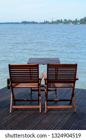 Two Wooden Chairs On The Dock Near The Water. A Metaphor For Waiting An Ideal Partner, An Online Love Life. Lost Souls, Virtual Conversations.
