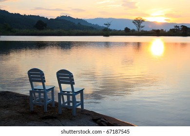 Two Wooden Chairs On The Lake And Sunset