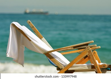 Two Wooden Deck Chairs With Towels Slung Over Them Sit On Florida Beach.