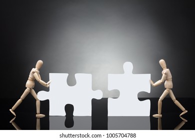 Two Wooden Dummies Solving White Jigsaw Puzzle On Grey Background - Powered by Shutterstock