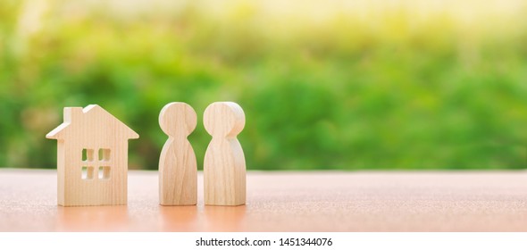 Two wooden figures of people and a house on a nature background. concept of affordable housing, mortgages for buying a home for young families and couples. Family nest. Copy space. Banner