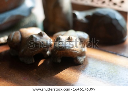 Two wooden frogs places together on the table with sunlight shining to them from the glass window, its background is wooden table