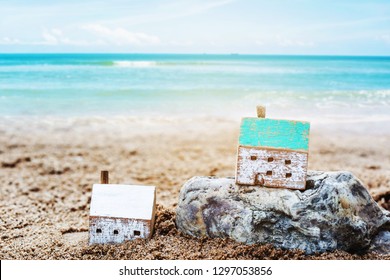 Two Wooden houses model on the rock and sand with blurred seascape background, Christian concept wise man build house on the rock but foolish man built house on the sand