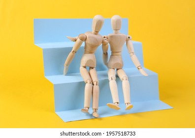 Two Wooden puppets hug on stairs podium, yellow background. Concept art, minimalism